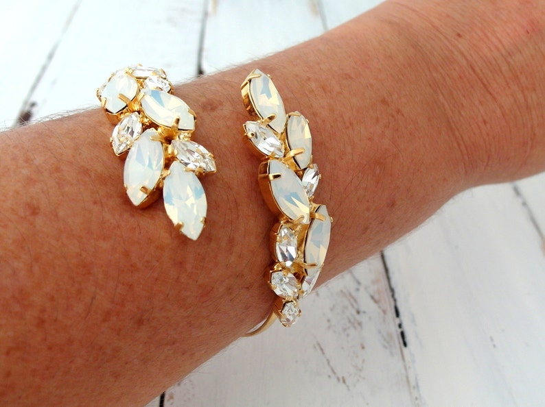 May include: A gold cuff bracelet with a design of white opal-like stones arranged in a leaf pattern.