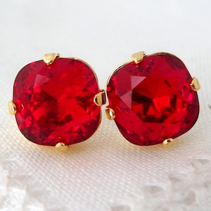 Könnte beinhalten: Ein Paar goldene Ohrstecker mit roten quadratischen Edelsteinen.
