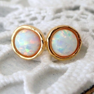 May include: A pair of gold stud earrings with white opal stones. The earrings have a textured gold setting.