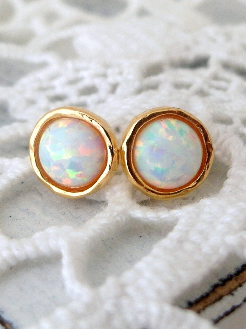 May include: A pair of gold stud earrings with white opal stones. The earrings have a textured gold setting.