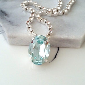 May include: A silver chain necklace with a large oval-shaped light blue crystal pendant.