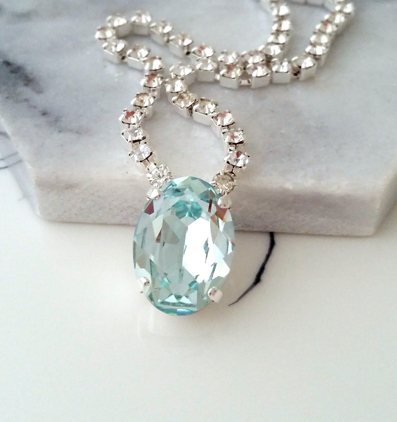 May include: A silver chain necklace with a large oval-shaped light blue crystal pendant.