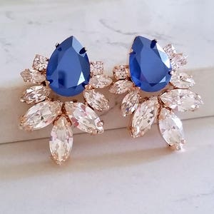May include: A pair of rose gold earrings with a large blue teardrop-shaped crystal surrounded by smaller clear crystals.