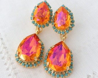 May include: A pair of dangle earrings with two teardrop-shaped orange and pink iridescent stones. The stones are surrounded by a turquoise blue beaded border.