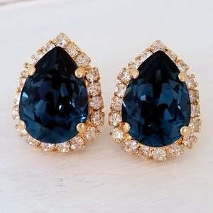 May include: A pair of gold tone earrings with a teardrop shaped blue crystal surrounded by smaller clear crystals.