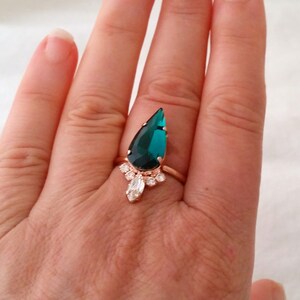 May include: A teardrop-shaped emerald green ring with a rose gold band and smaller clear stones around the main stone.