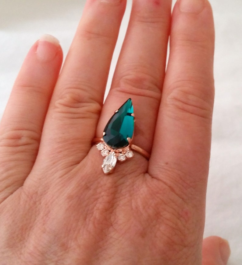 May include: A teardrop-shaped emerald green ring with a rose gold band and smaller clear stones around the main stone.