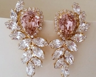 Puede incluir: Un par de pendientes de oro con un gran cristal rosa en el centro y cristales transparentes más pequeños que lo rodean. Los pendientes están diseñados con un racimo de cristales transparentes que caen en cascada desde el cristal central.