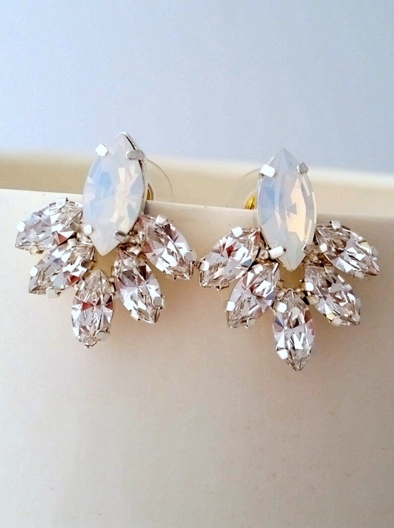 May include: A pair of silver earrings with a large, white, marquise-shaped crystal in the center and smaller, clear, marquise-shaped crystals surrounding it.