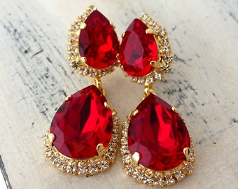 May include: A pair of dangle earrings with large teardrop-shaped red crystals surrounded by a halo of smaller clear crystals. The earrings are gold-toned.