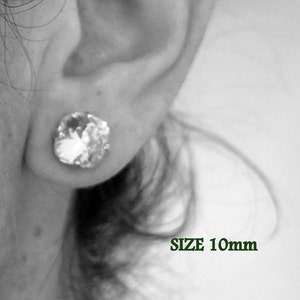 Puede incluir: Primer plano de la oreja de una persona con un pendiente de cristal transparente. El pendiente tiene un tama&ntilde;o de 10 mm. Debajo del pendiente se escribe SIZE 10mm.