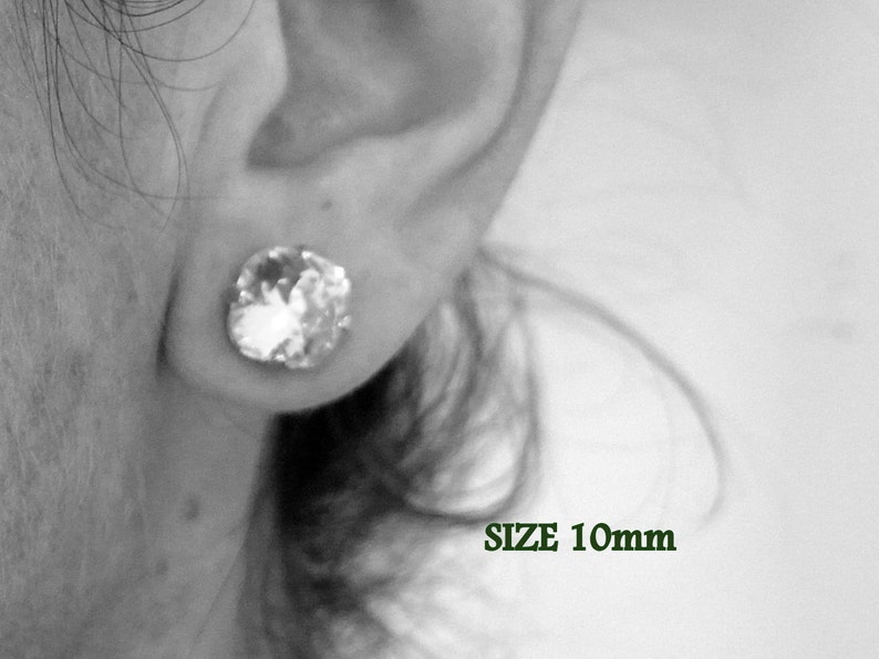 Puede incluir: Primer plano de la oreja de una persona con un pendiente de cristal transparente. El pendiente tiene un tama&ntilde;o de 10 mm. Debajo del pendiente se escribe SIZE 10mm.
