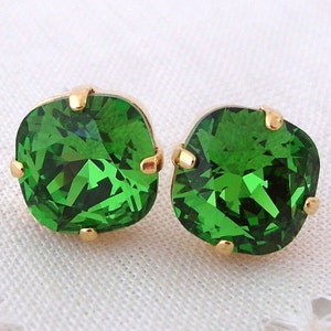 May include: A pair of gold stud earrings with emerald green square-shaped gemstones.