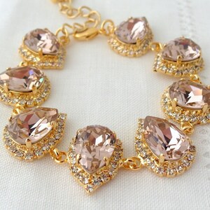 May include: A gold bracelet with a teardrop-shaped crystal design. The crystals are a light blush pink color and are set in a gold metal frame. The bracelet is made of a chain link design.