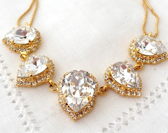 May include: A gold necklace with five teardrop-shaped clear crystals. Each crystal is surrounded by a gold setting with smaller clear crystals.