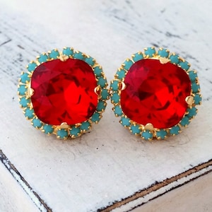以下が含まれることがあります： 大きな正方形の赤い宝石がターコイズの石のハローで囲まれた、赤とターコイズのイヤリングのペアです。