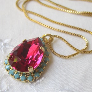 May include: A gold chain necklace with a pink teardrop-shaped crystal pendant surrounded by turquoise blue crystals.