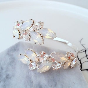May include: A silver bangle bracelet with a cluster of white opal and clear crystal stones arranged in a leaf design.