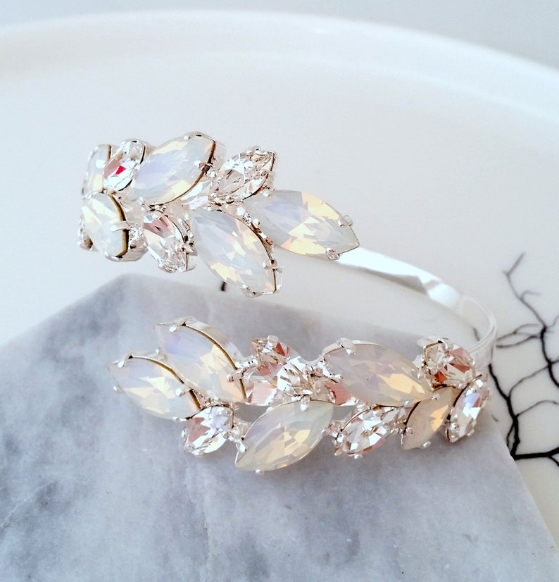 May include: A silver bangle bracelet with a cluster of white opal and clear crystal stones arranged in a leaf design.