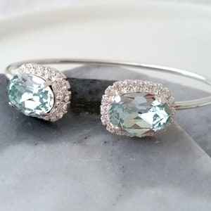 May include: A silver bangle bracelet with two oval-shaped blue gemstones set in a halo of smaller clear stones.