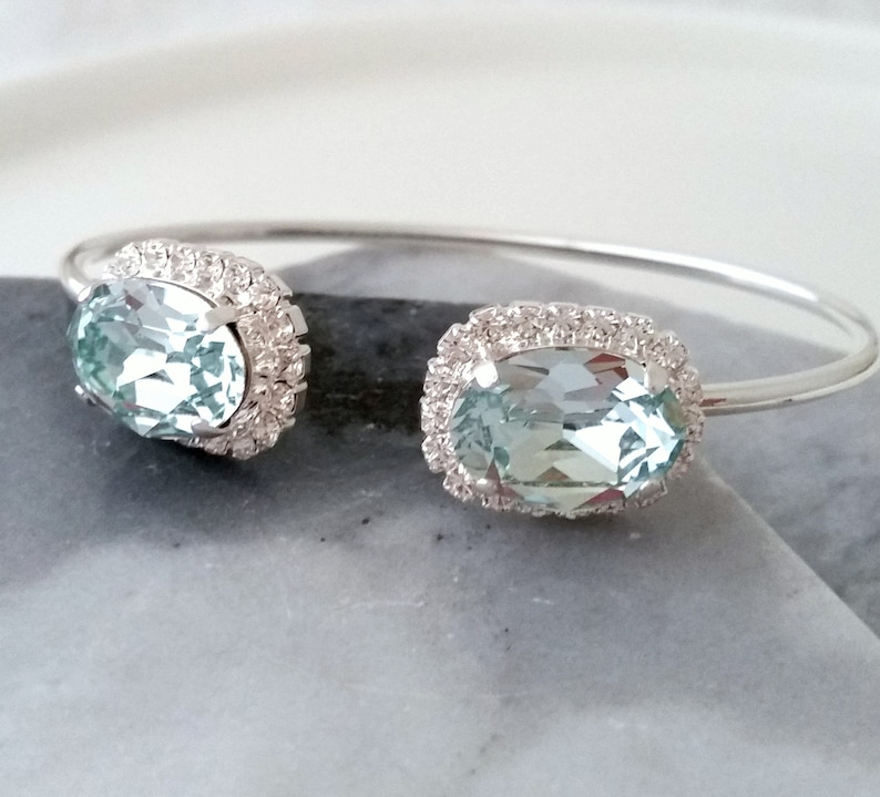 May include: A silver bangle bracelet with two oval-shaped blue gemstones set in a halo of smaller clear stones.