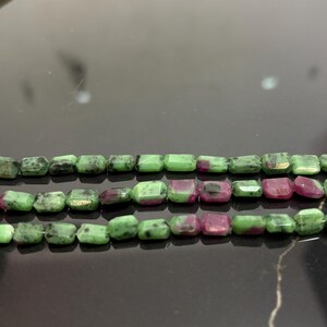 Könnte beinhalten: Drei Stränge aus Edelsteinperlen. Die Perlen sind eine Mischung aus Grün und Rot und haben eine quadratische Form. Die Perlen sind zu einer Halskette oder einem Armband aufgereiht.