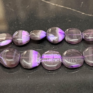 May include: A strand of smooth, flat, circular beads featuring a translucent purple and grey banded pattern. The beads are arranged in two horizontal rows, displaying a polished finish with visible internal layers and the text RhiannaGems.