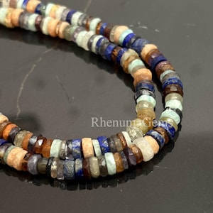 May include: Close-up of two strands of gemstone beads. The beads are a mix of colours, including blue, orange, brown, and green. The beads are small and faceted, creating a sparkling effect. The beads are strung together, forming a necklace or bracelet.