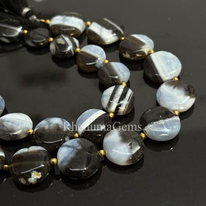 May include: Close-up of a strand of gemstone beads. The beads are a mix of black, white, and gray, with a flat, round shape. The beads are strung together with gold-colored accents and a black tassel.