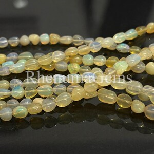 May include: Strands of polished, oval-shaped opal beads in shades of yellow, cream, and pale blue. The beads are strung together, creating a textured and colorful display. The image is well-lit, highlighting the opalescent quality of the gemstones.