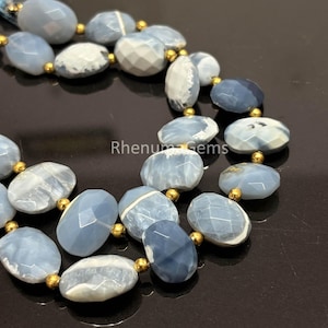 May include: A strand of faceted, oval-shaped light blue and white gemstone beads interspersed with small, round, metallic gold-colored spacer beads. The text RhenumGems is visible in the center of the image among the beads.