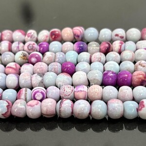 May include: Close-up of strands of round beads in shades of pink, purple, and white. The beads have a marbled appearance, with variations in color and pattern. The beads are strung together, creating a textured surface.