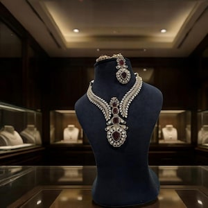 Può includere: Un set di collana e orecchini esposto su un manichino nero. I gioielli presentano un metallo color argento con pietre preziose chiare e rosse. La collana ha un design floreale con un grande pendente. L'orecchino è un bottone abbinato.