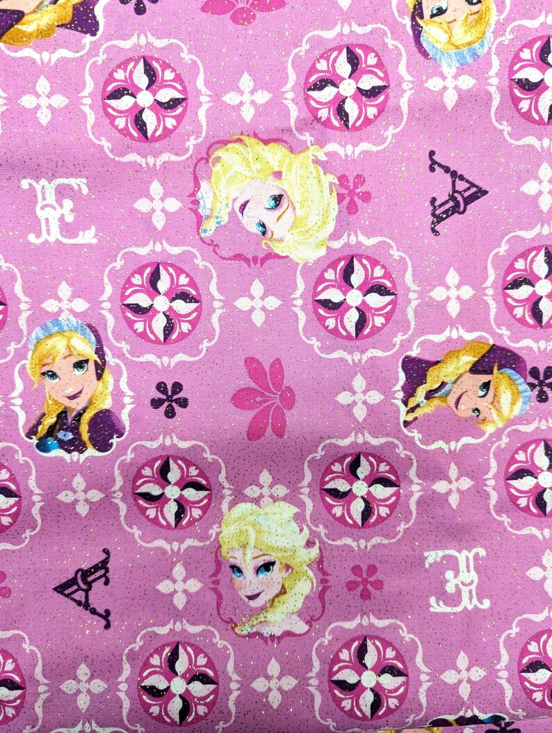 May include: Pink fabric with a repeating pattern featuring cartoon character portraits, floral designs, and decorative elements. The design includes portraits of a blonde character with blue eyes, set against a background of white and dark pink shapes.