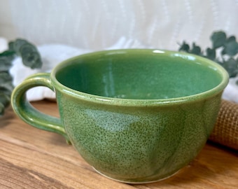 Può includere: Una tazza in ceramica verde con una glassa macchiettata. La tazza ha una forma arrotondata e un manico.