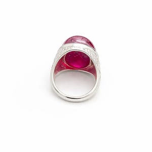 Może przedstawiać: Srebrny pierścionek z dużym, owalnym, przezroczystym, r&oacute;żowym kamieniem szlachetnym. Obręcz pierścionka jest gładka, a oprawa wok&oacute;ł kamienia ma szczeg&oacute;łowy, grawerowany wz&oacute;r. Kamień szlachetny ma żywy, nasycony r&oacute;żowy kolor.