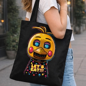 May include: Black tote bag featuring a cartoon chicken character with yellow, blue, red, and brown accents. The text "LET'S EAT!!!" is displayed in colorful letters on the character's shirt.