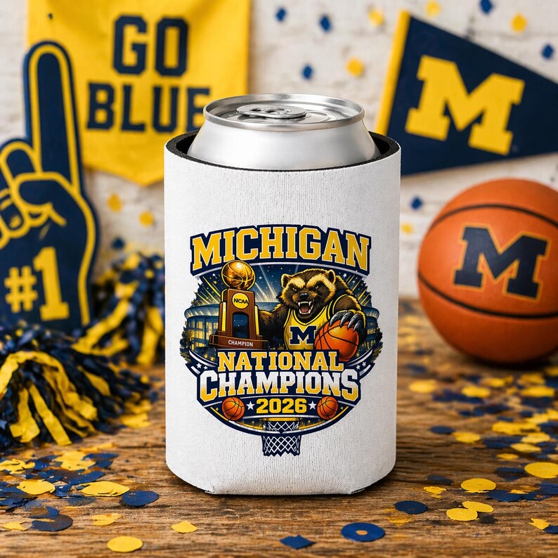 Puede incluir: Un enfriador de latas blanco con el texto "MICHIGAN NATIONAL CHAMPIONS 2026" y un tej&oacute;n de dibujos animados sosteniendo una pelota de baloncesto. Una pelota de baloncesto y banderines con la letra "M" est&aacute;n en el fondo. El enfriador est&aacute; dise&ntilde;ado para mantener las bebidas fr&iacute;as.