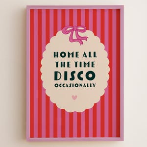 May include: Framed art print with a pink and red striped background. The print features the text "HOME ALL THE TIME DISCO OCCASIONALLY" in black and green, with a pink bow and a small pink heart. The frame is pink.