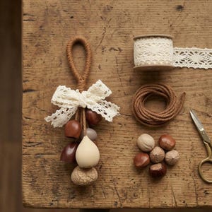 May include: A collection of craft supplies on a wooden surface. Includes a decorative hanging ornament with a lace bow, a spool of lace trim, a coil of twine, a pair of scissors, and several decorative wooden beads and nuts.