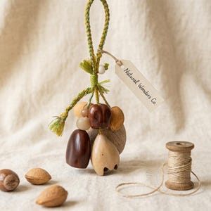 Puede incluir: Adorno de madera artesanal con un cordón trenzado verde y amarillo y una etiqueta que dice "Natural Wonders Co.". El adorno presenta varias formas y cuentas de madera en tonos marrón y beige. También hay un carrete de hilo y nueces.