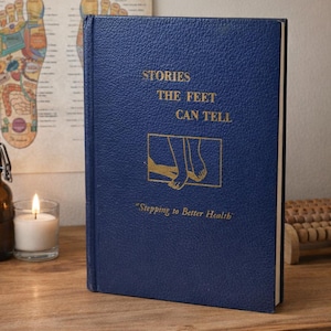 May include: A navy blue book titled "Stories the Feet Can Tell" with gold lettering and an illustration of feet. A reflexology chart and a candle are in the background. The book's subtitle reads "Stepping to Better Health."