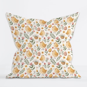 Op de afbeelding: Een decoratief kussen met een herhalend patroon van gele kuikens, paaseieren, bloemen en groen op een witte achtergrond. Het kussen heeft een unieke vorm met puntige randen. Het ontwerp doet denken aan de lente en Pasen.