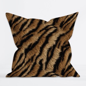 Può includere: Cuscino decorativo quadrato con motivo a righe di tigre. Il cuscino presenta un design a righe marrone e nero, che imita l'aspetto della pelliccia di tigre. Il cuscino è di forma quadrata e viene probabilmente utilizzato per l'arredamento della casa.