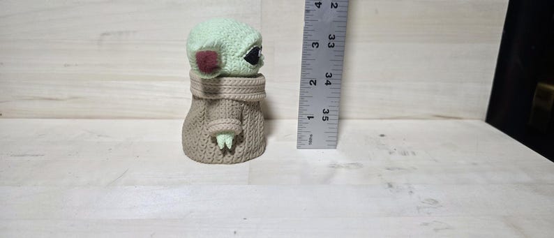 May include: A small, light green figurine of a character with large black eyes and pointed ears, wearing a tan robe. The figurine is approximately 3.5 inches tall. The character's head is light green with a red patch on each cheek.