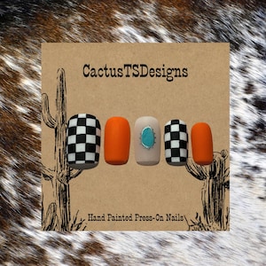 May include: A set of press-on nails with a variety of designs. The nails feature a checkerboard pattern, solid orange, and a neutral nail with a turquoise stone. The card reads "CactusTSDesigns" and "Hand Painted Press-On Nails".