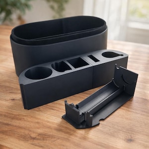 May include: A black car organizer set with multiple compartments and cup holders. The set includes a large rectangular bin, a smaller organizer with various slots, and a separate tray. The items are made of a matte black material.