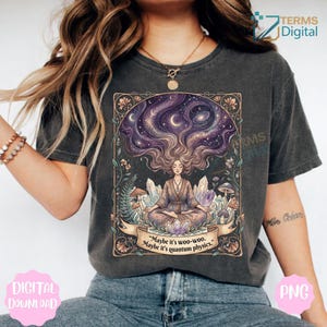 Puede incluir: Camiseta gris oscuro con una ilustración detallada de una figura meditando con cabello suelto, un cielo estrellado y cristales. El diseño incluye el texto "Maybe it's woo-woo. Maybe it's quantum physics."