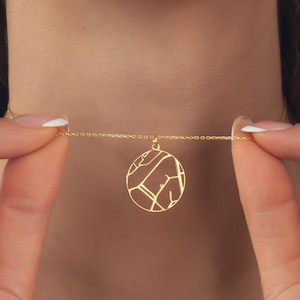 May include: A gold-colored necklace with a circular pendant featuring a map-like design. The delicate chain is held between two hands, showcasing the pendant's intricate details. The necklace is a stylish accessory.