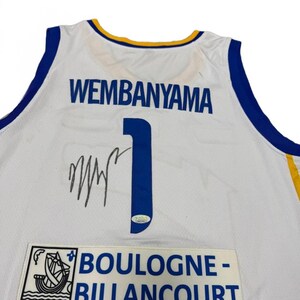 May include: White basketball jersey with blue and gold accents. The jersey features the name "WEMBANYAMA" in blue block letters, the number "1", and a signature. A patch at the bottom reads "BOULOGNE-BILLANCOURT".